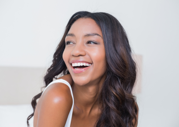 The image shows a woman with long, wavy hair laughing and looking off to the side, showcasing a bright smile against a light background.