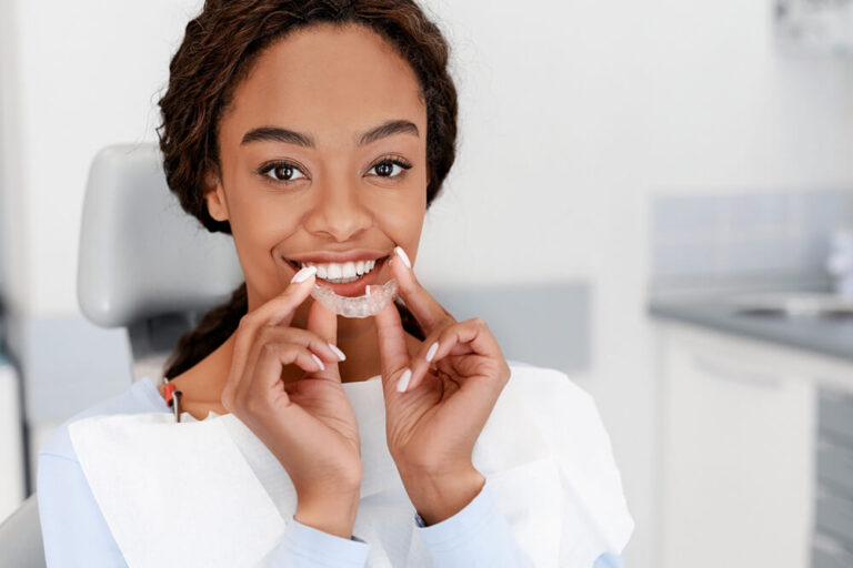 Patient seated in a dental clinic holding a clear orthodontic aligner near their mouth, wearing a dental bib—illustrating modern teeth-straightening treatment with invisalign.