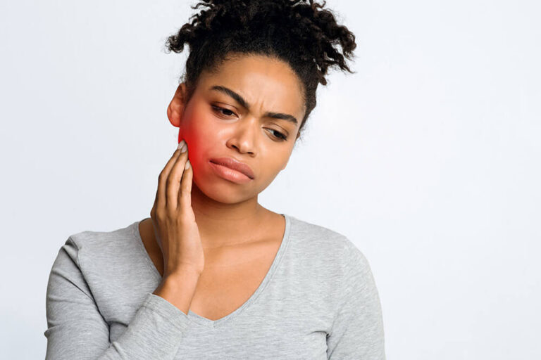 Woman touching her cheek with visible redness, showing discomfort from toothache or jaw pain, illustrating dental emergency or oral health issue.